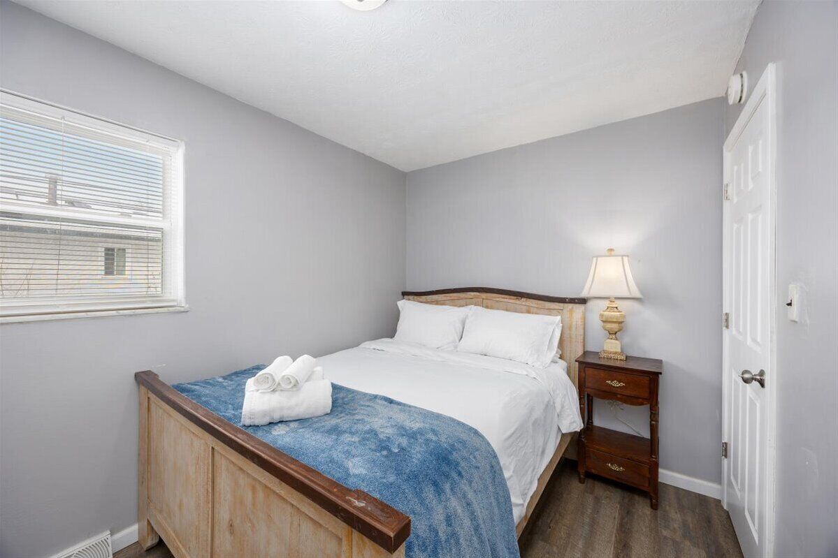 A bedroom with a single bed, a nightstand with a lamp, and a window with blinds.
