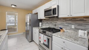 Una cucina moderna con mobili bianchi, un frigorifero in acciaio inossidabile, un forno a microonde, un piano cottura a gas e un tostapane.