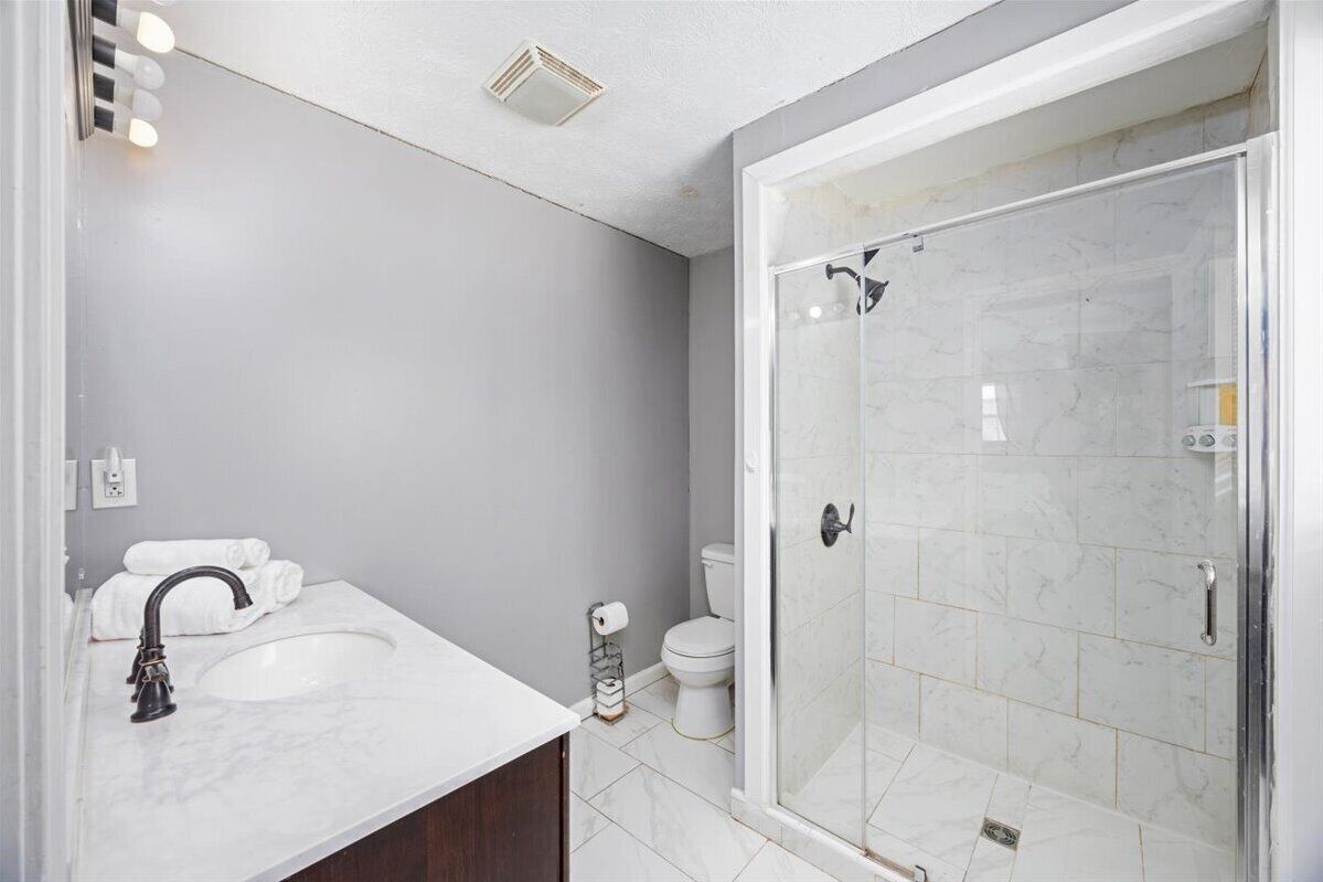 A modern bathroom with a white sink, a toilet, and a glass-enclosed shower.