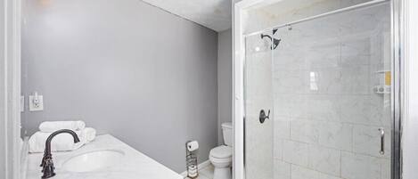 A modern bathroom with a white sink, a toilet, and a glass-enclosed shower.