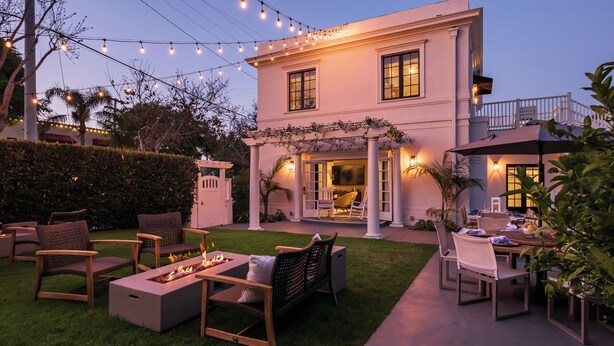 Una casa de dos pisos con un patio que cuenta con mobiliario exterior, una chimenea y luces colgantes.
