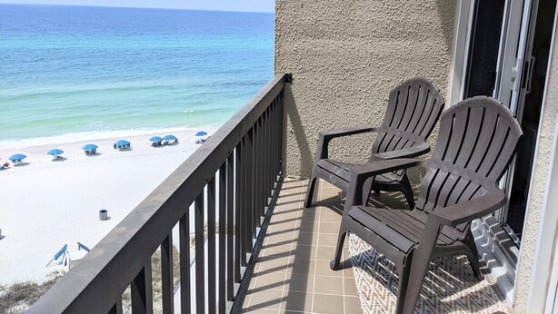 A balcony with two Adirondack chairs overlooking a beach with blue umbrellas.