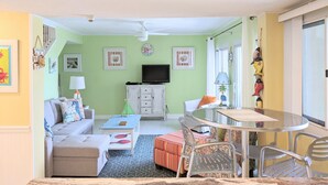 A living room with a sofa, a coffee table, a TV, and a dining area with a table and chairs.