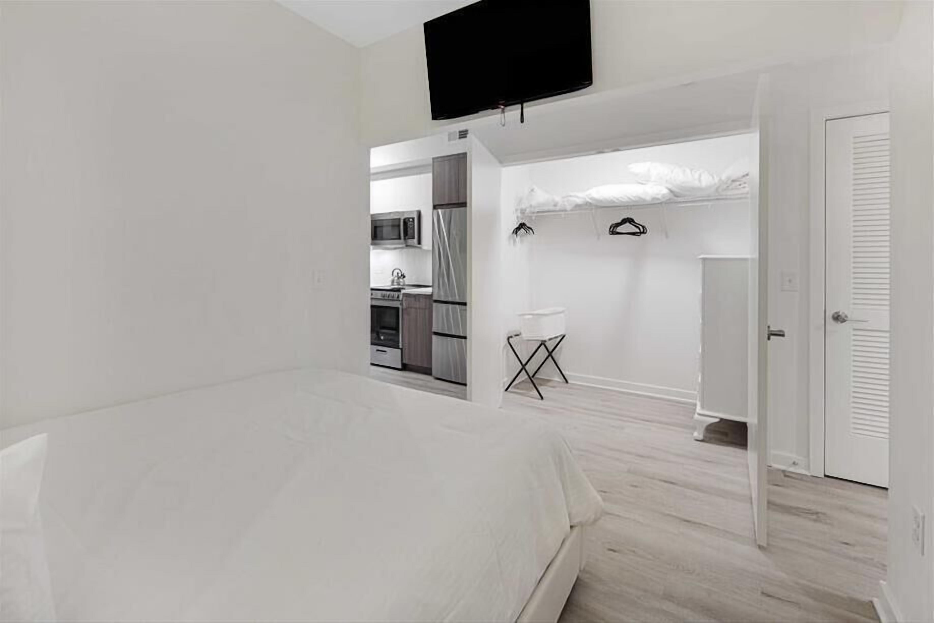 Un dormitorio moderno con una cama, un televisor en la pared y vistas a una zona de cocina.