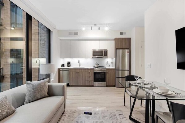 A modern kitchen with stainless steel appliances, a dining area with a glass table, and a sofa with patterned cushions.