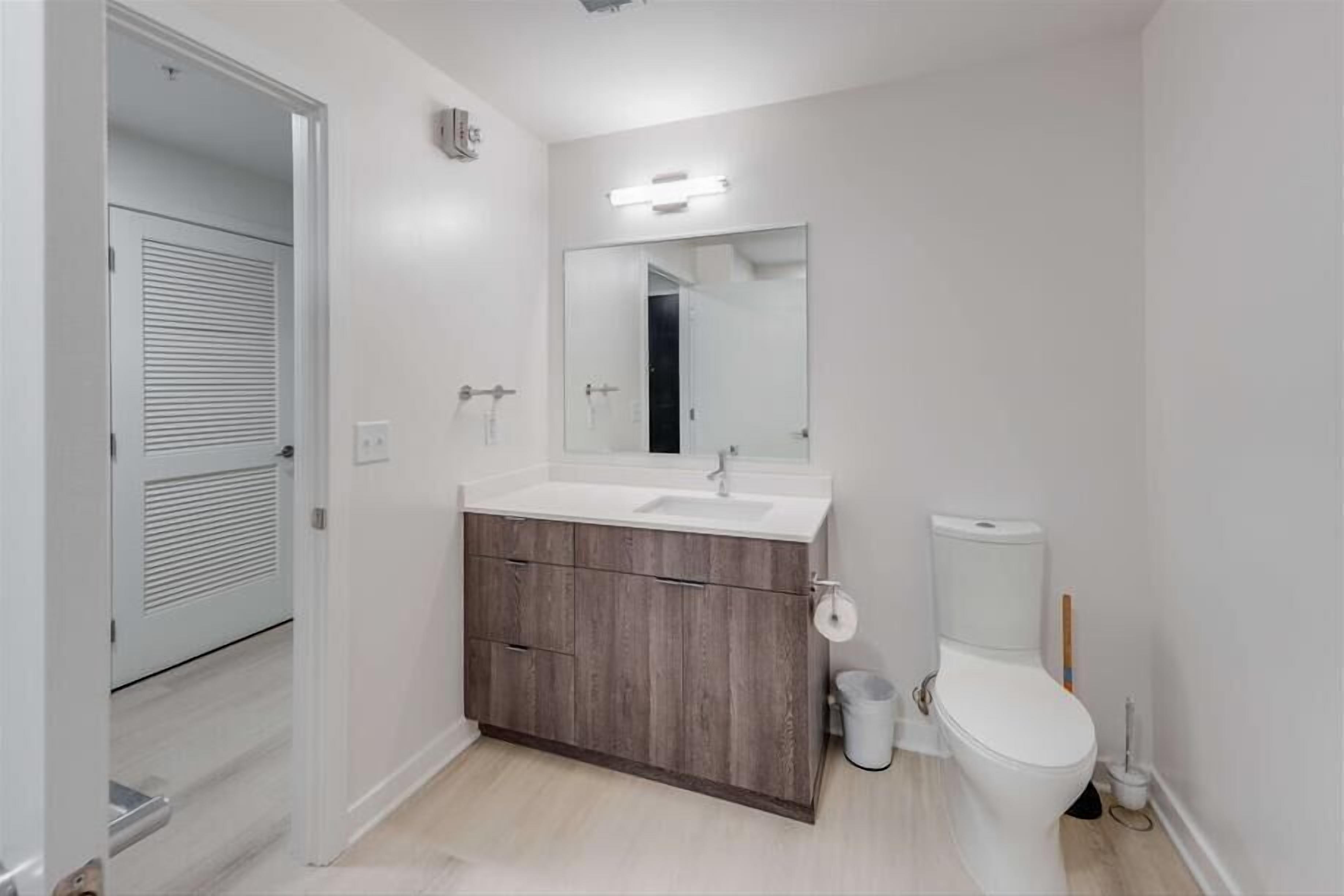 A modern bathroom with a wooden vanity, a large mirror, and a toilet.