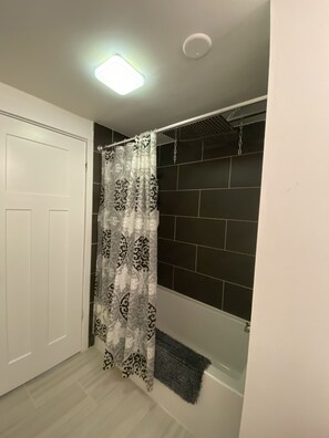 Een badkamer met douchegordijn, een witte deur, een badkuip en een betegelde muur.