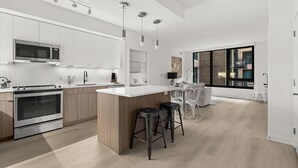 Une cuisine moderne dotée d’un îlot central, d’appareils électroménagers en acier inoxydable et d’une grande fenêtre qui laisse entrer la lumière naturelle.