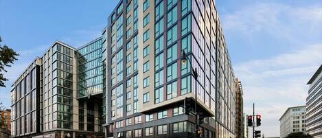 A modern building with multiple floors, large windows, and a prominent entrance with a sign.
