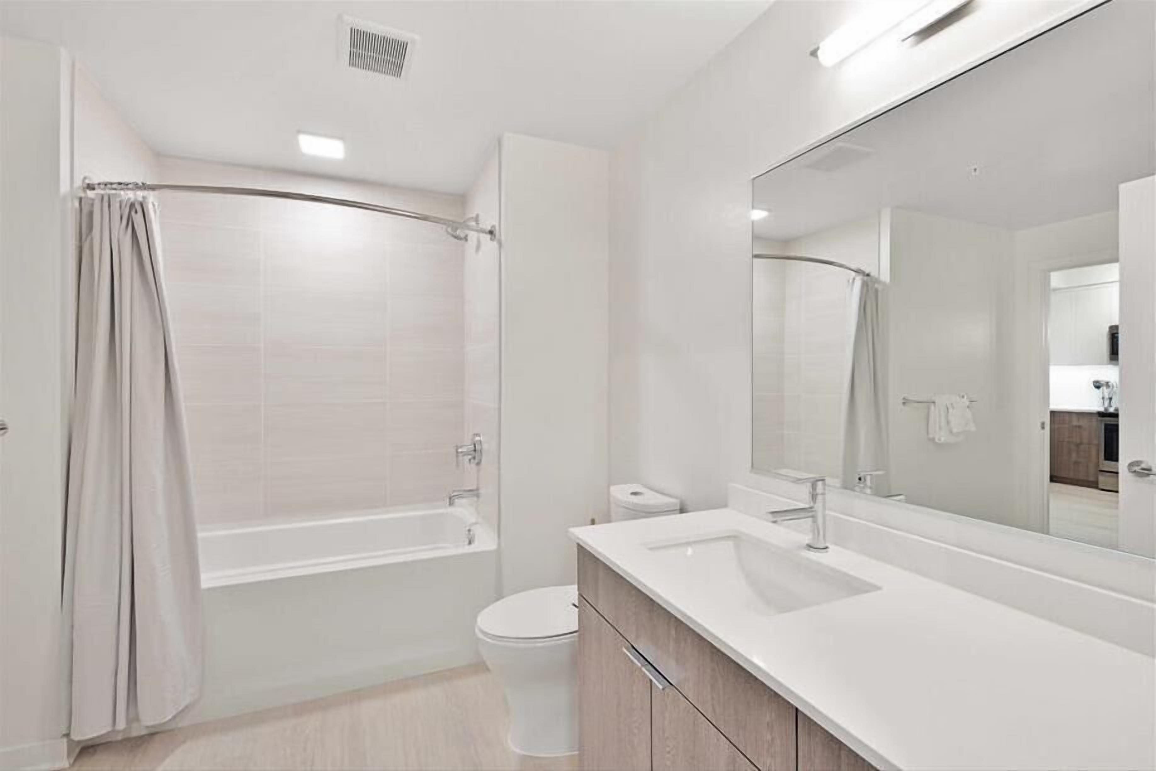 A modern bathroom with a bathtub, toilet, and a large mirror.