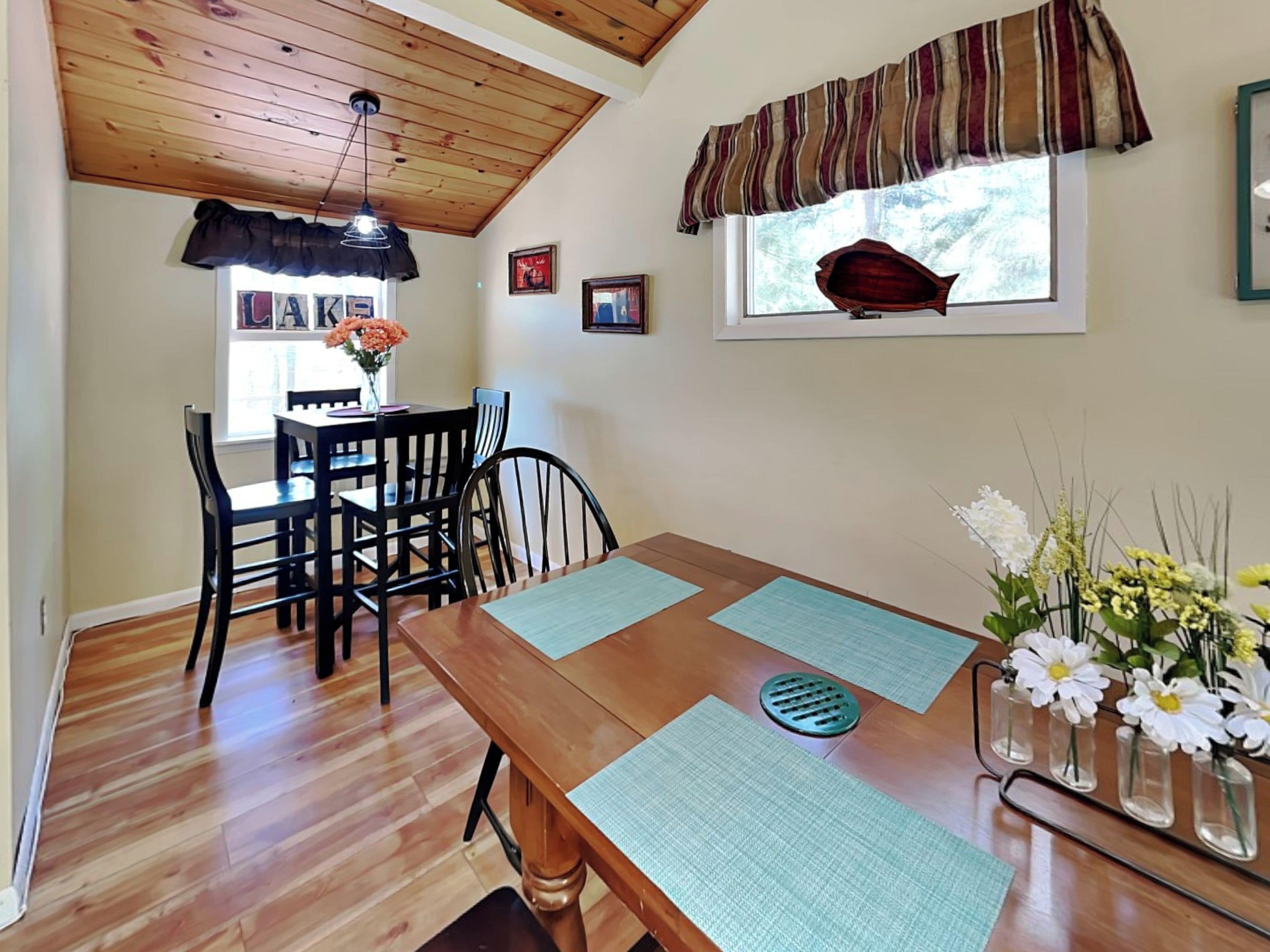 A dining area with a wooden table, chairs, and a window with a view of trees.