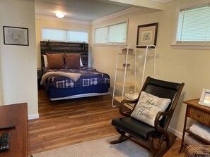 A bedroom with a bed, a chair with a pillow, a bedside table, and a window. - Summer Days Winter Nights by Taylor Made Deep Creek (Swanton)