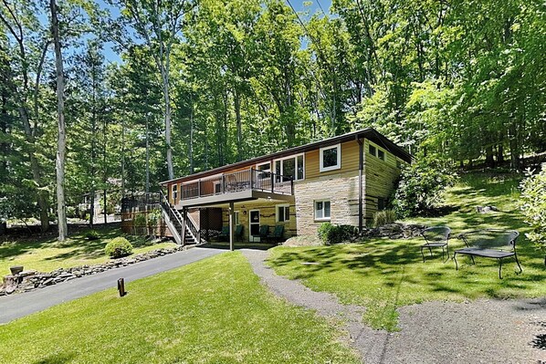 Une maison à deux étages avec un balcon, entourée d’arbres et d’une pelouse bien entretenue.