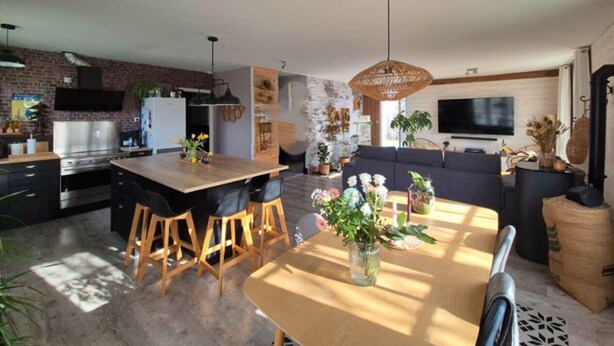 A modern kitchen with a central island, bar stools, a dining table with a vase of flowers, and a large TV mounted on the wall. - A 3-star family-run inn with a pool: "La Parenthèse," just outside La Rochelle (Villedoux)
