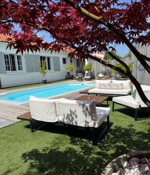 Un jardin avec une piscine, un espace salon extérieur et une maison en arrière-plan.