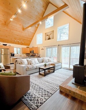 A cozy living room with a fireplace, a sofa, and a kitchen in the background. - Family Retreat | Game Room + Firepit | Sleeps 10 (Conway)