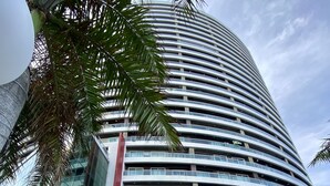 A modern, multi-story building with a curved facade, large glass windows, and a central entrance area with potted plants.