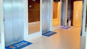 A hotel lobby with a tiled floor, elevators, and a reception area.