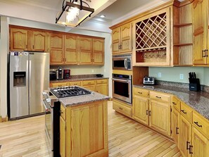 Eine Küche mit Holzausstattung, einem Edelstahlkühlschrank, einem Gasherd, einem Backofen und einer Mikrowelle.
