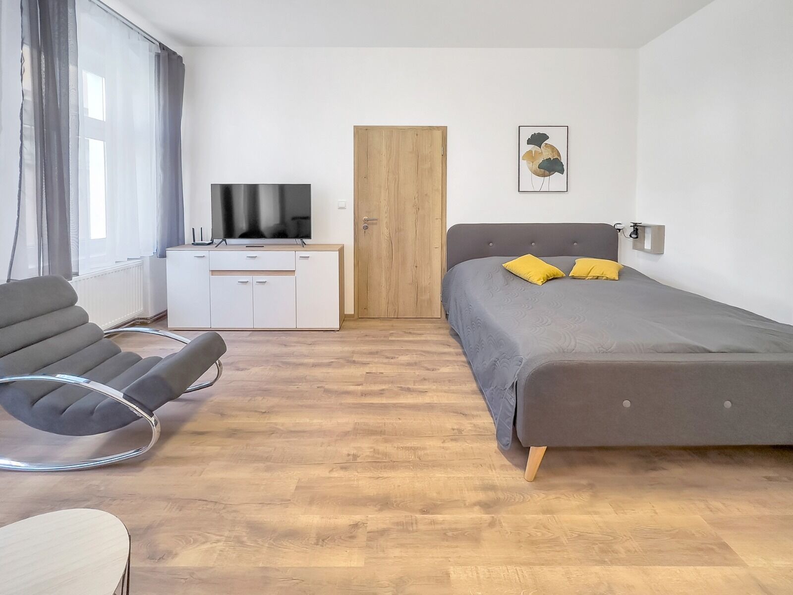 A modern bedroom with a bed, a desk, a chair, and a television.