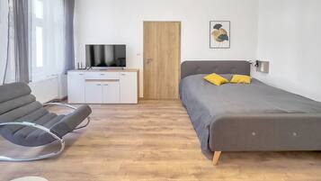 A modern bedroom with a bed, a desk, a chair, and a television.