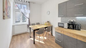 Una cuina moderna amb armaris grisenys, una taula de menjador de fusta i una finestra amb cortines transparents.