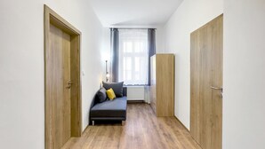 Un passadís estret amb un sofà i un radiador al fons, portes de fusta a banda i banda, i una finestra amb cortines.