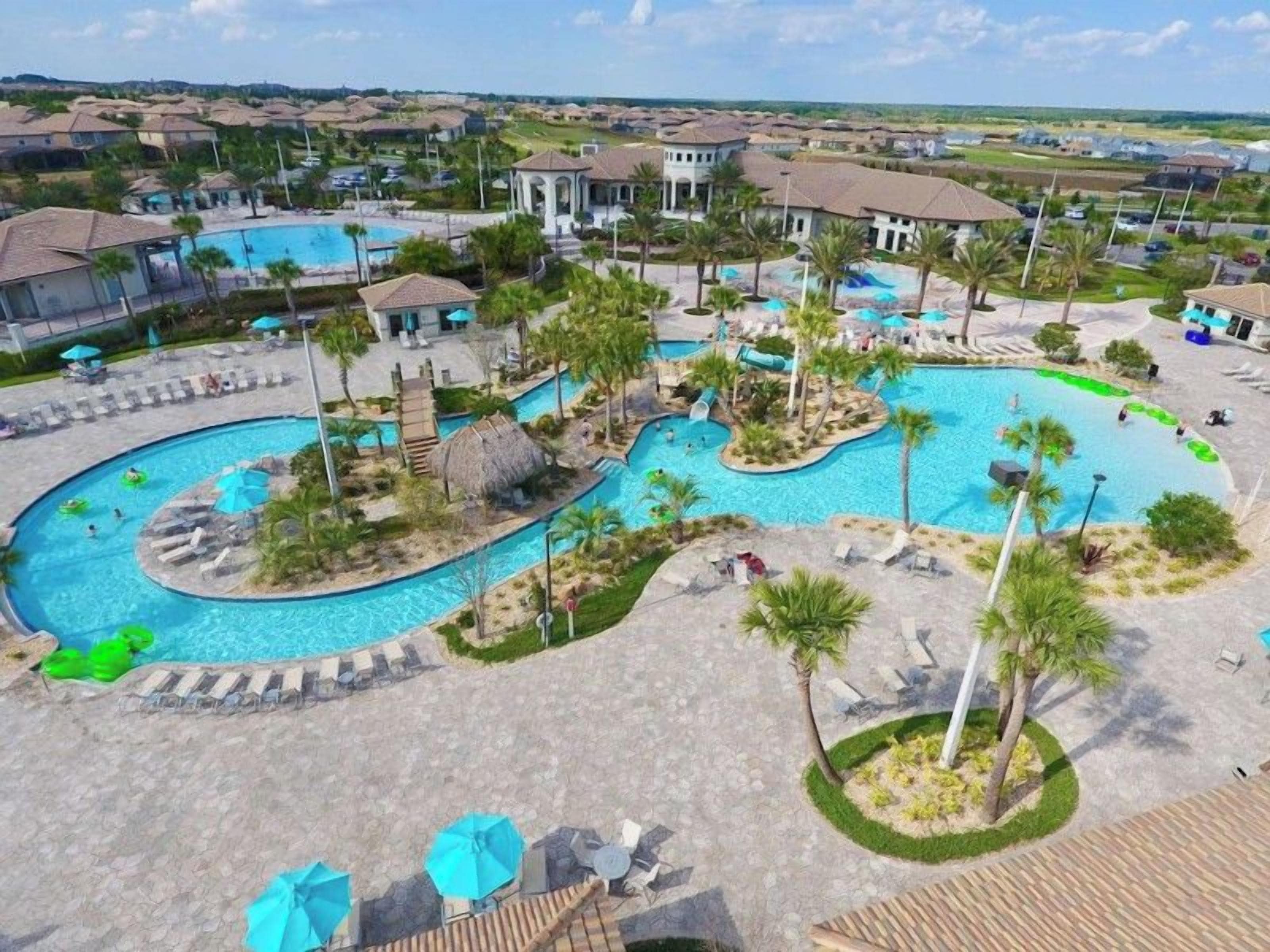 A resort with a large swimming pool, lounge areas, and a view of the surrounding neighborhood.