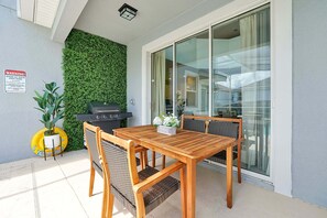 Une terrasse extérieure avec une table et des chaises en bois, un barbecue et un mur végétal.
