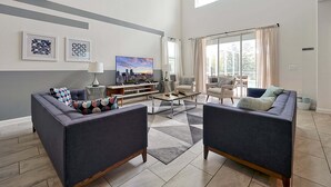 Amplia sala de estar con un ventanal grande, televisor de pantalla plana y una zona de estar con dos sofás y una mesa de centro.