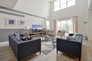 Ein geräumiges Wohnzimmer mit großem Fenster, einem Flachbildfernseher und einer Sitzecke mit zwei Sofas und einem Couchtisch.
