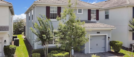 A residential building with a tiled roof, a garage, and a well-maintained lawn with a small tree.
