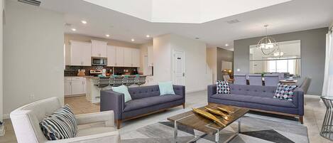 A modern living room with a sofa, armchair, coffee table, and a dining area with a chandelier.