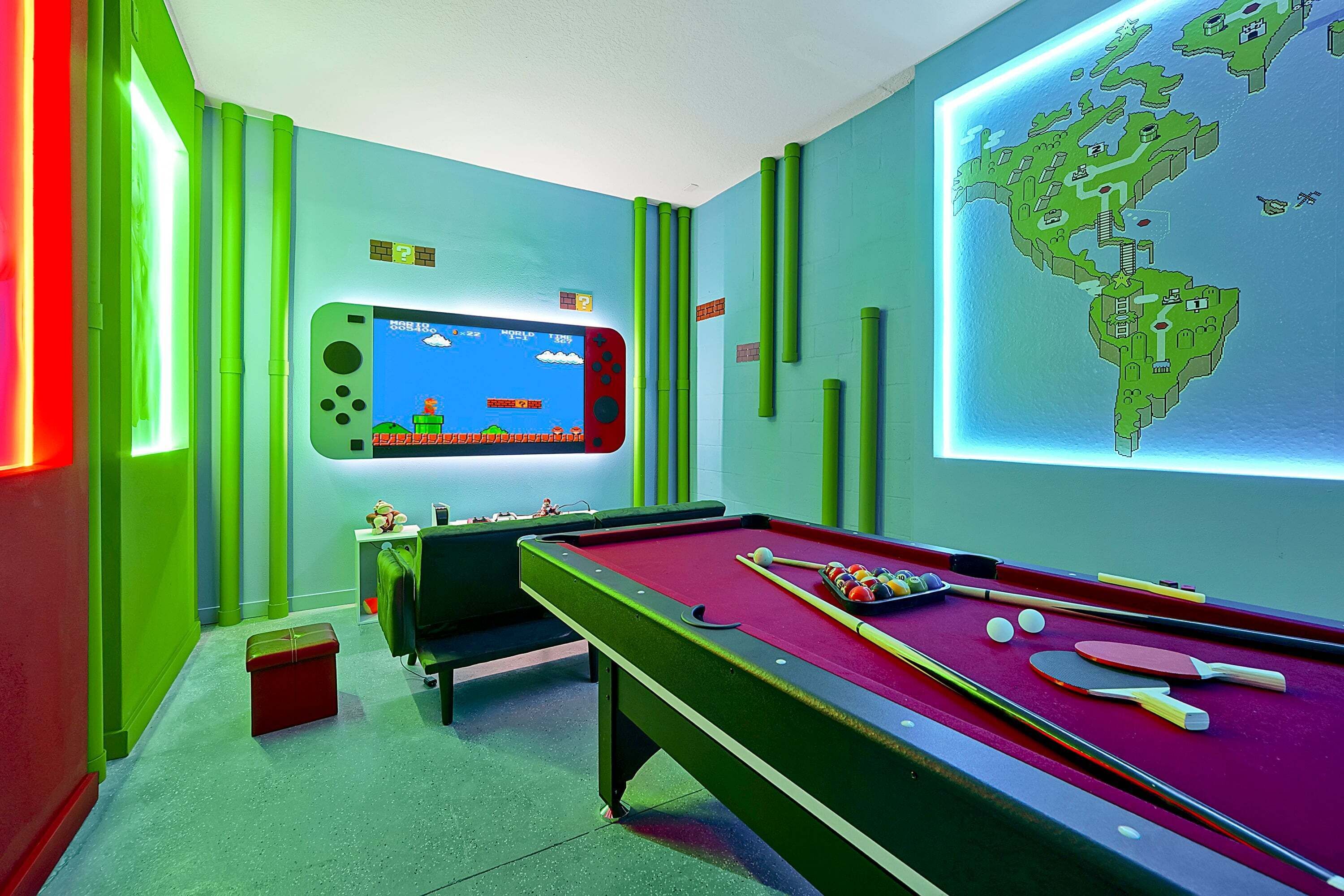 A pool table with billiard balls and cues, a Nintendo Switch with a game on the screen, and a map on the wall.