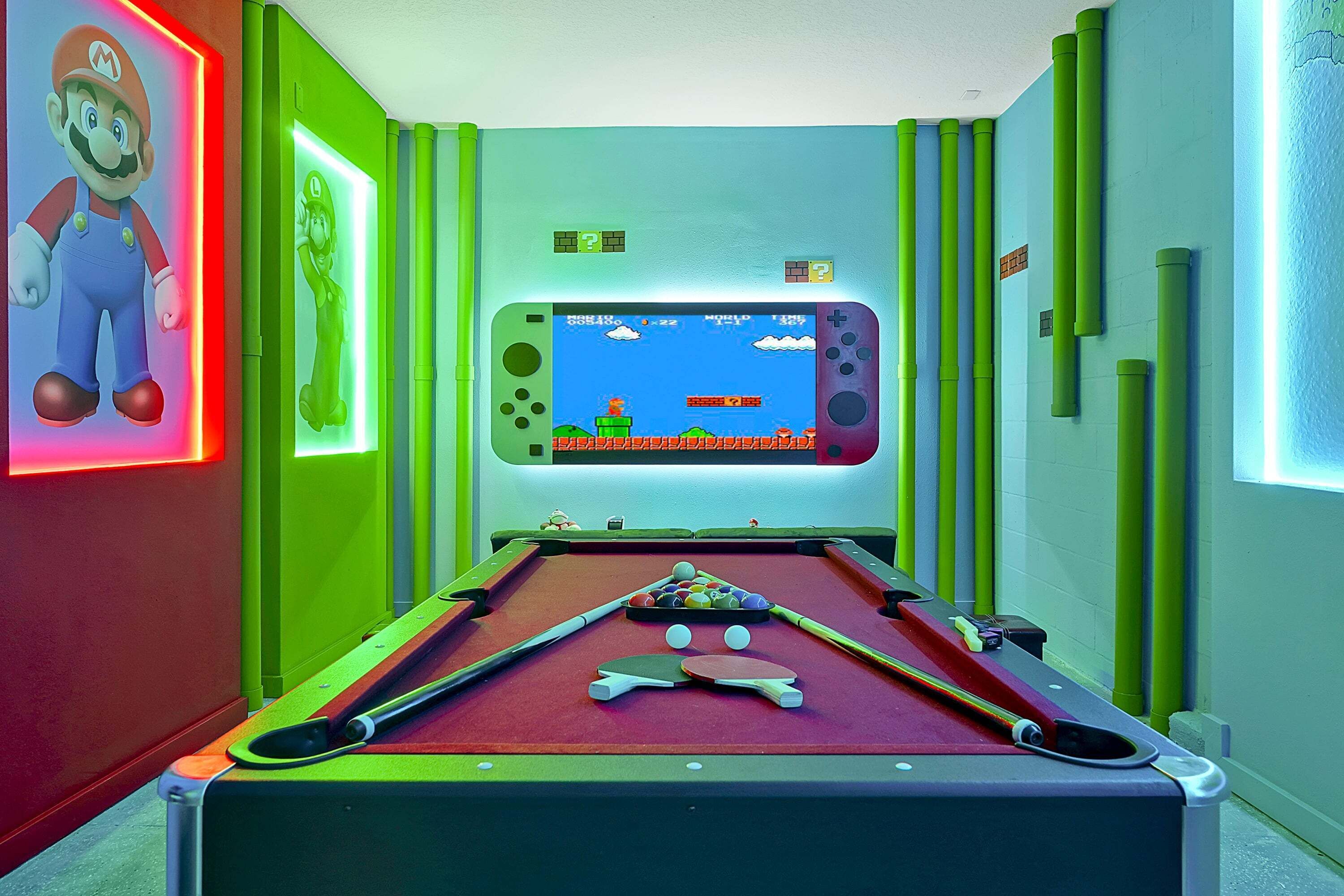 A pool table with a video game screen, green walls, and Mario-themed decorations.