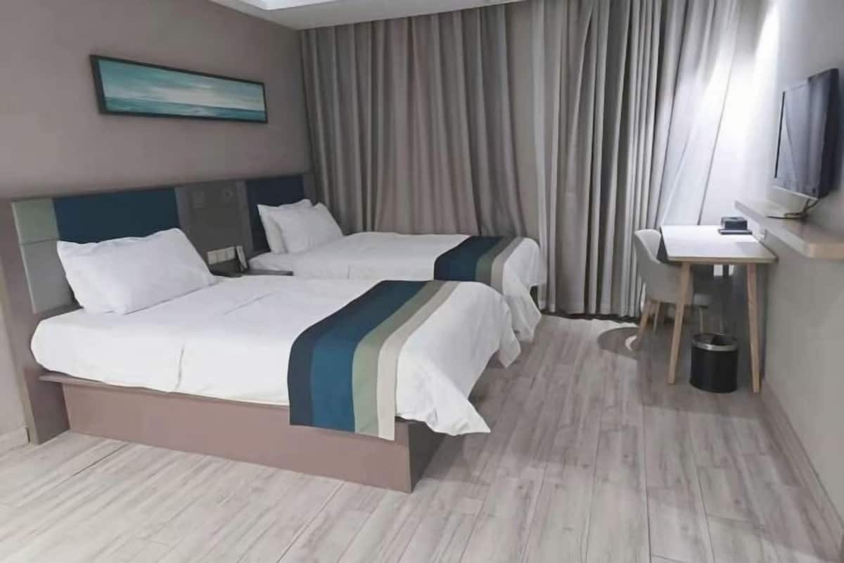 A hotel room with two beds, a desk, a TV, and a painting on the wall.