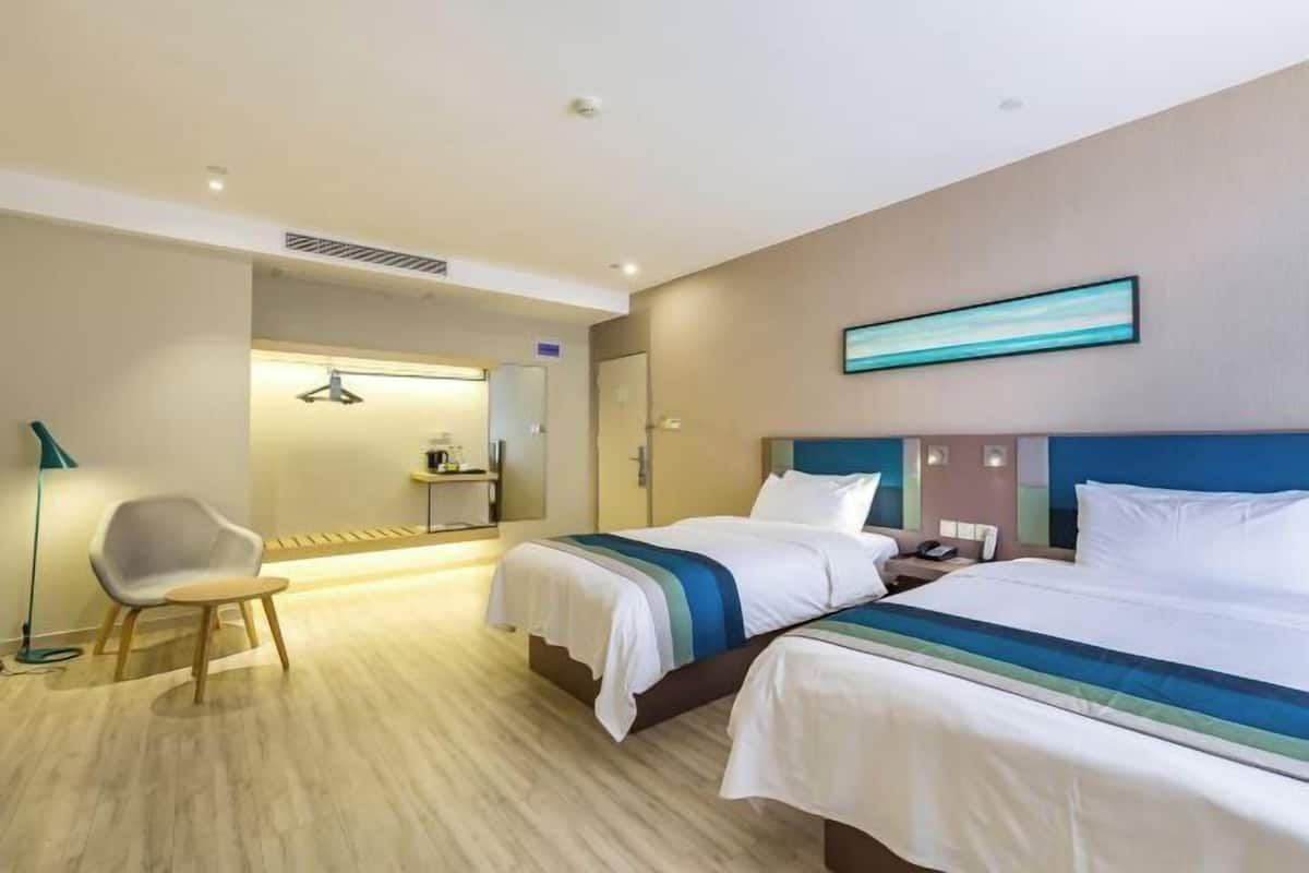 A hotel room with two beds, a desk, a chair, and a painting on the wall.