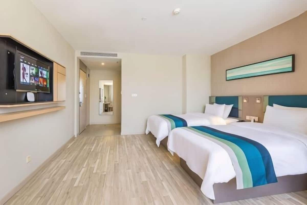 A hotel room with two beds, a TV, and a hallway leading to a bathroom.