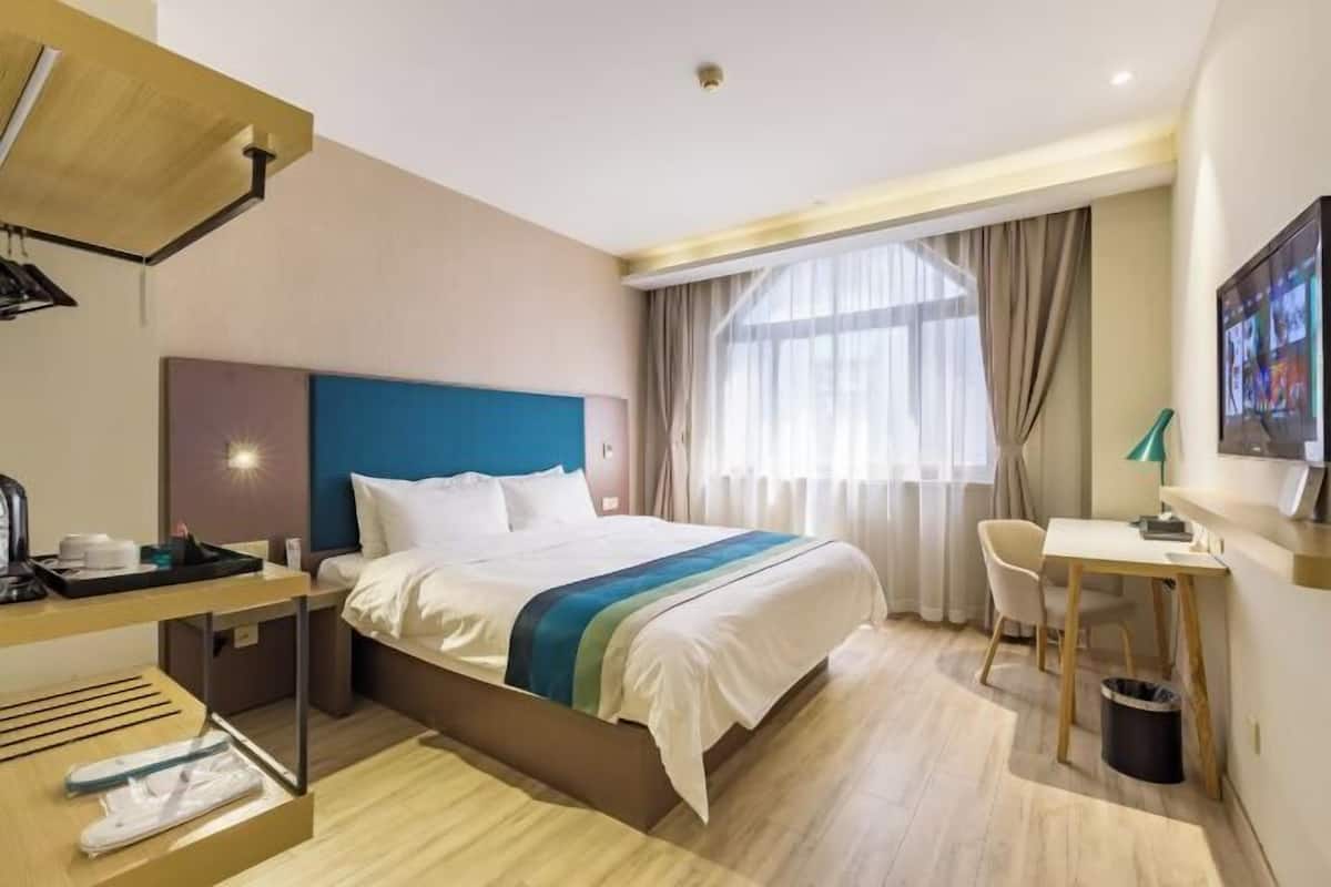 A hotel room with a bed, desk, chair, and a TV on the wall.