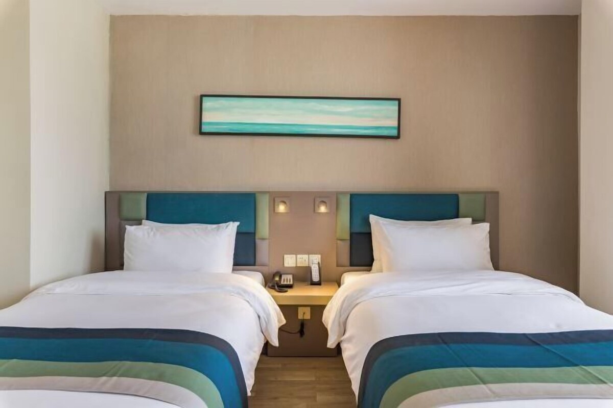 A hotel room with two beds, a nightstand, a phone, and a painting on the wall.