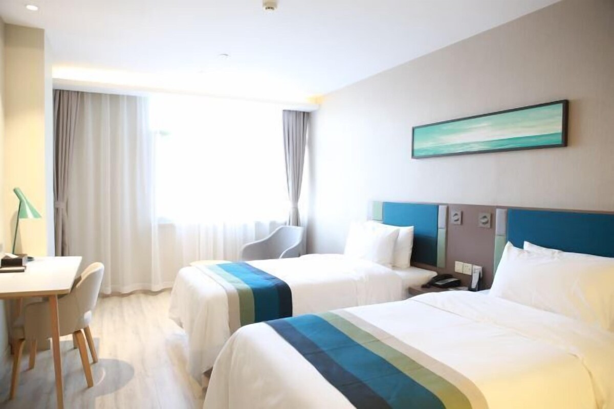 A hotel room with two beds, a desk, a chair, and a window with curtains.