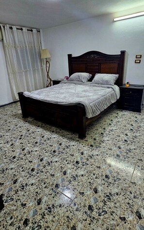 A bedroom with a bed, a nightstand, a lamp, and a tiled floor. - Bahaa (Jerash)