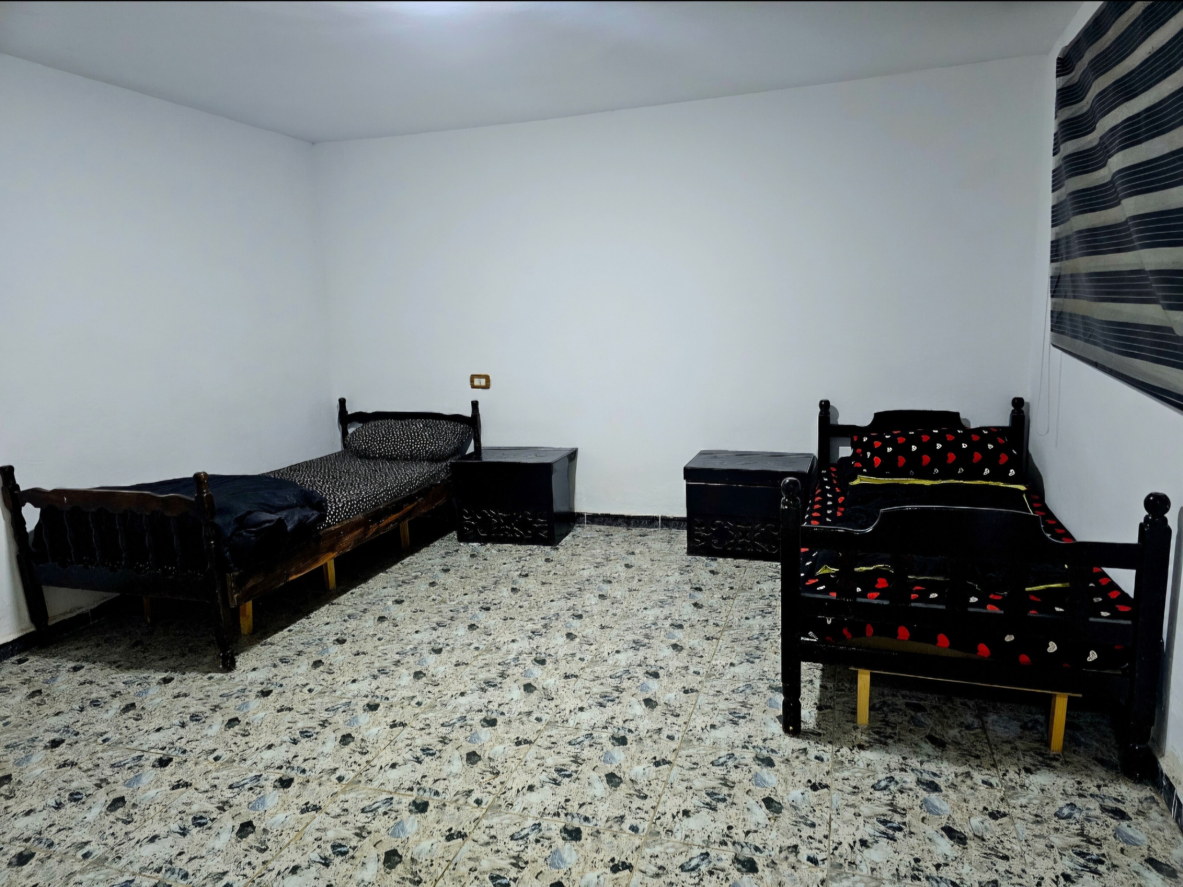 Ein Schlafzimmer mit zwei hölzernen Betten, einem kleinen Nachttisch, einem Beistelltisch und einem Fliesenboden.