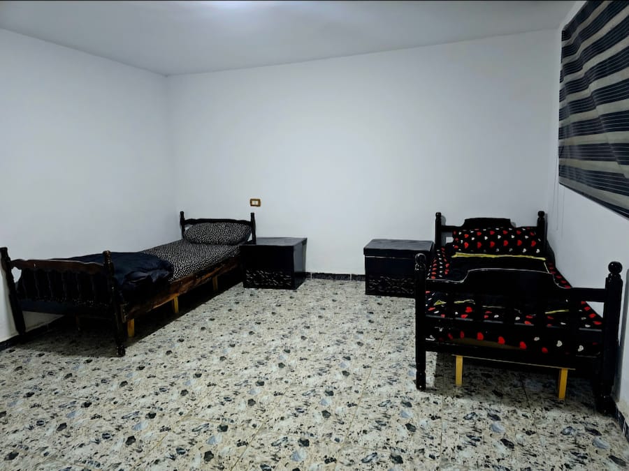 A bedroom with two wooden beds, a small bedside table, a nightstand, and a tiled floor.