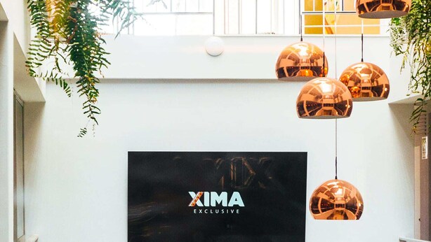 A multi-level atrium with hanging copper globes, a large XIMA Exclusive sign, and indoor plants. - Xima Central Tacna (Tacna)