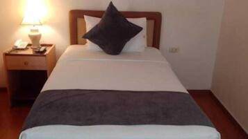 A neatly made bed with a white and gray bedspread, a dark pillow, and a wooden headboard. There is a nightstand with a lamp and a phone beside the bed.