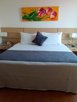 A hotel room with a bed, a nightstand, a lamp, and a painting of flowers on the wall. - Xima Central Tacna (Tacna)