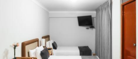 A hotel room with two single beds, a flat-screen TV mounted on the wall, a wooden nightstand, a small table with a vase, and a red door.
