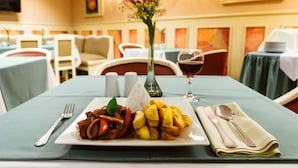 A dining table with a plate of food, a glass of red wine, and a vase of flowers. - Xima Central Tacna (Tacna)