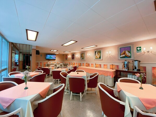 Un restaurante con varias mesas y sillas, un televisor en la pared y obras de arte en las paredes.